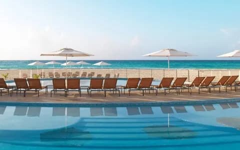 A swimming pool with a row of lounge chairs look onto the sea at Playacar Palace. A swimming pool with a row of lounge chairs look onto the sea at Playacar Palace.