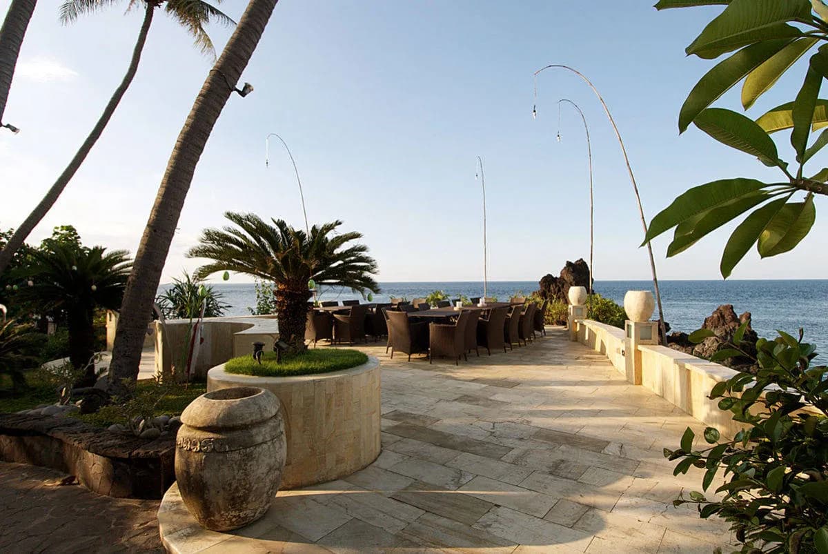 Dining tables sit on a stone terrace next to the coastline at Alam Batu Beach Bungalow Resort Bali Dining tables sit on a stone terrace next to the coastline at Alam Batu Beach Bungalow Resort Bali