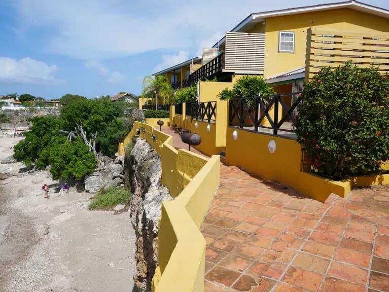 A sunny beachfront apartment with a yellow facade and a pathway leading to it. A sunny beachfront apartment with a yellow facade and a pathway leading to it.