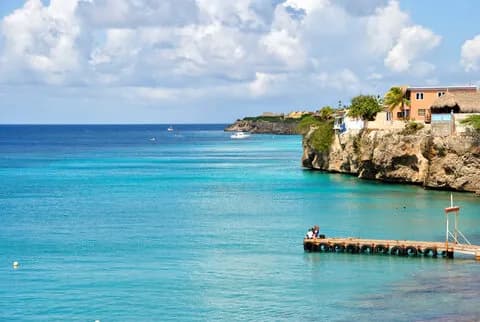 A serene ocean view with a dock and apartments perched on the coastline, creating a picturesque coastal scene. A serene ocean view with a dock and apartments perched on the coastline, creating a picturesque coastal scene.