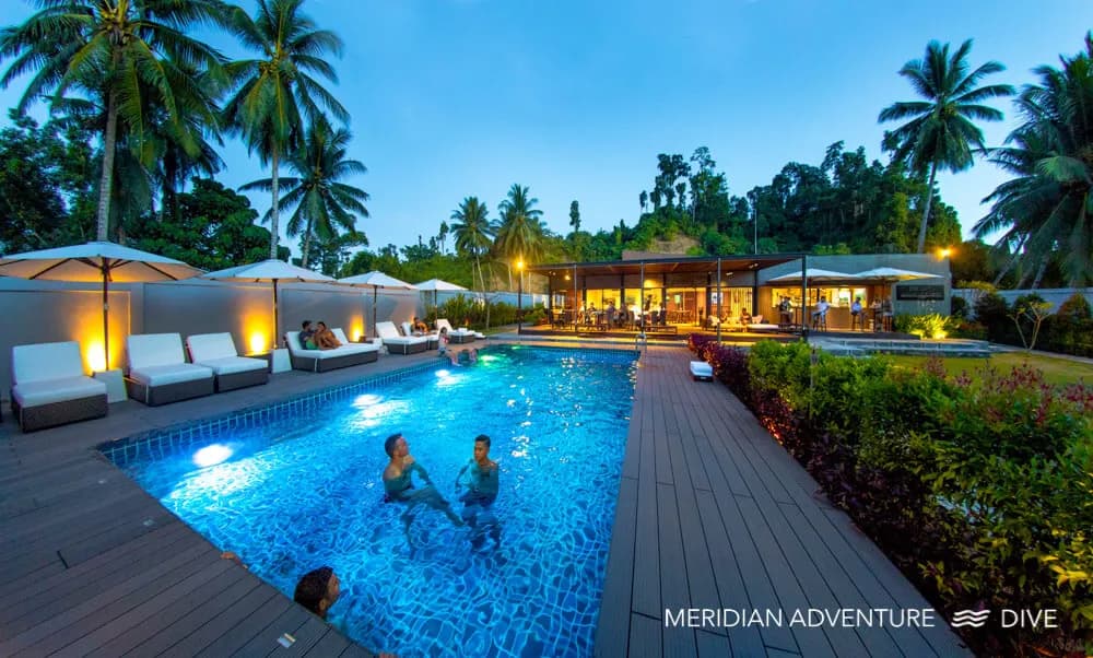a swimming pool at dusk with swimmers at Meridian Adventure Dive Resort & Marina Club a swimming pool at dusk with swimmers at Meridian Adventure Dive Resort & Marina Club