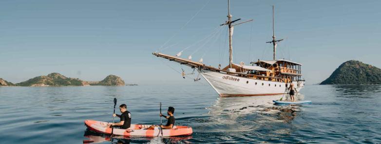 Two people kayaking with the phinisi in the background